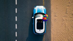 A Mini Cooper with colorful balloons drives along a desert road. Captured from above.